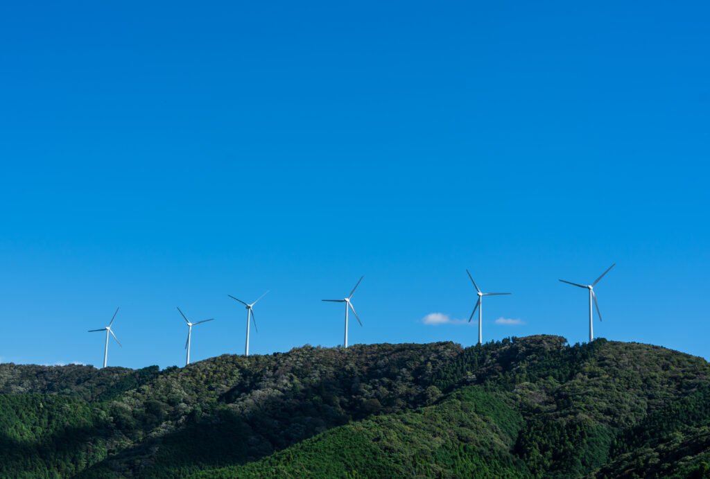 a spectacular landscape where multiple white wind turbines are lined up on a green mountain ridge beneath a vibrant blue sky. this view symbolically expresses the adoption of clean energy and commitme
